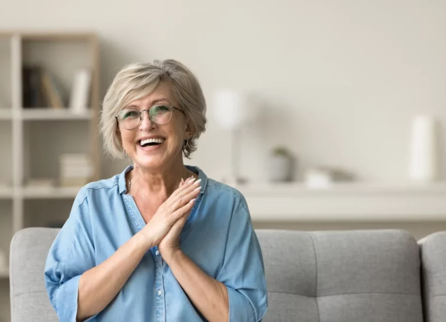 Smiling older woman with short gray hair and glasses sitting on a couch after Extractions at Gridley Dental.